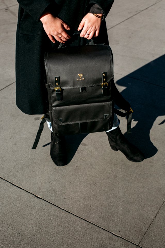 Person Wearing Black Coat Holing Black Leather Knapsack Backpack Standing On Concrete Ground photo