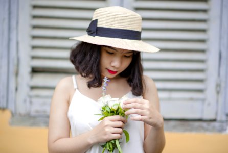 Woman Wearing Beige Sun Hat And White Sleeveless Top Holding White Flowers