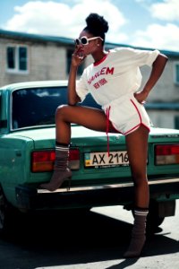 Photo Of Woman Wearing White Long-sleeved Shirt And White Dolphin Shorts With Red Trim Standing Near Teal Car photo