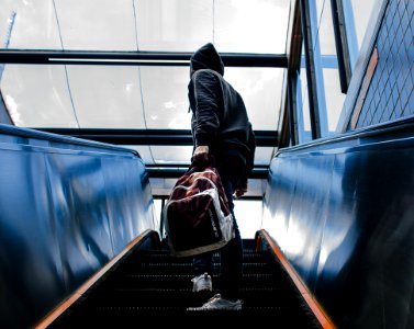 Person Wearing Black Hooded Jacket Standing On Escalator While Holding Backpack