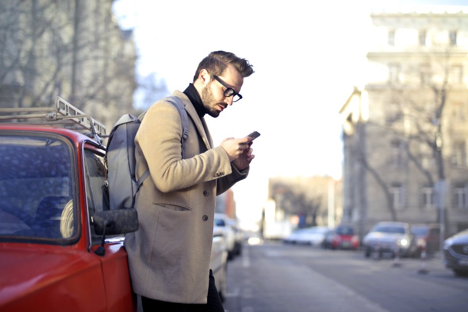 Man In Beige Coat Holding Phone Leaning On Red Vehicle photo