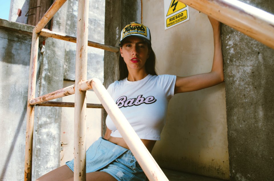 Woman In White Crew-neck Babe Printed Cap-sleeved Crop-top With Blue Denim Miniskirt Sitting Near Brown Metal Door