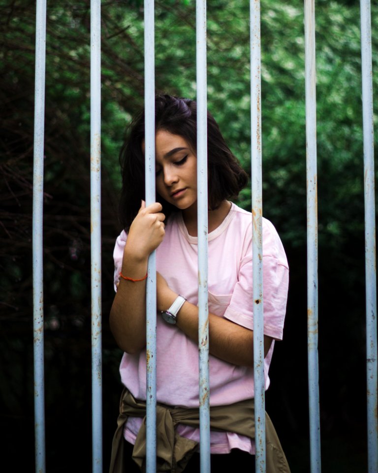 Woman Wearing Pink Crew-neck T-shirt Standing And Leaning Behind White Bars