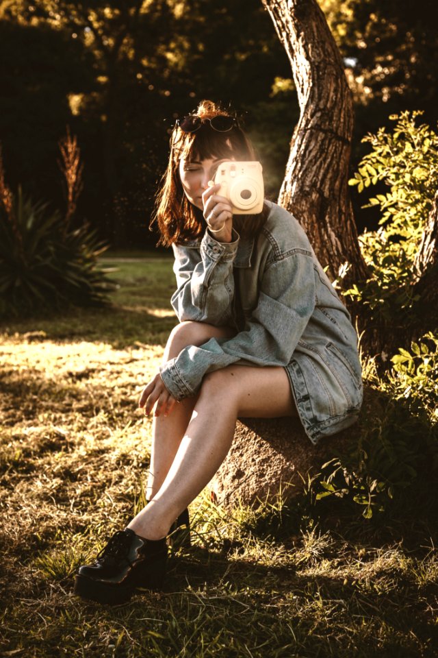 Woman Wearing Blue Denim Jacket Holding Pink Instant Camera Sitting On Soil