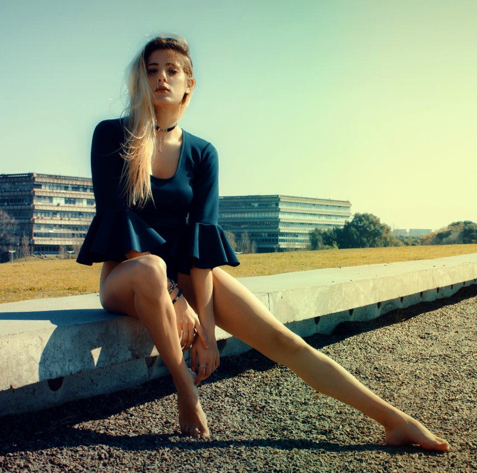 Woman Wears Black Scoop-neck Long-sleeved Blouse Seats On Grey Concrete Pavement