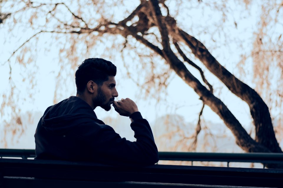 Man In Black Hoodie Sitting On Bench Near Green Trees