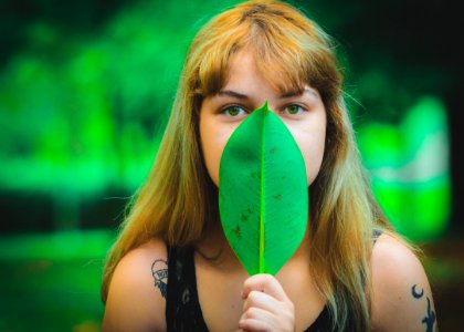 Woman Wearing Black Sleeveless Top Covering Mouth Using Green Leaf photo