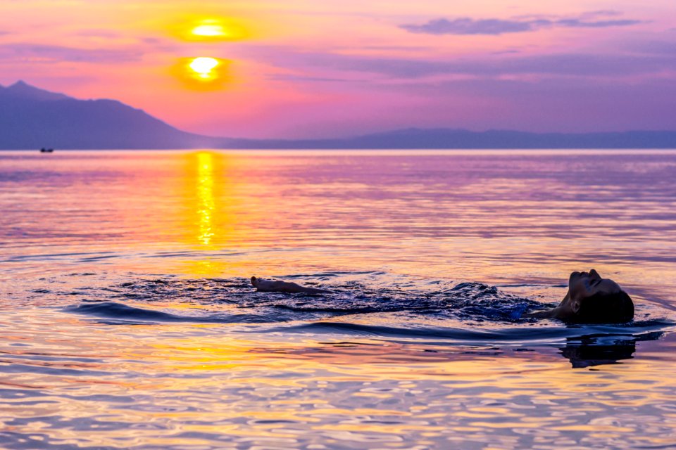 Person Swimming On Body Of Water During Golden Hour