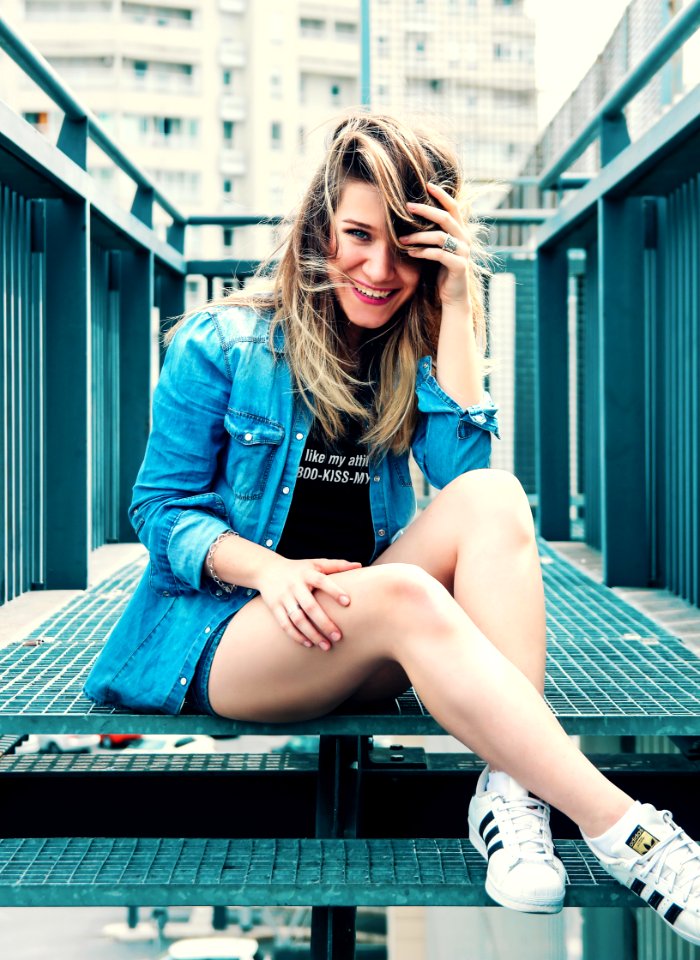 Woman Wearing Blue Denim Button-up Jacket And Black Printed Shirt With Pair Of White Adidas Superstar Shoes