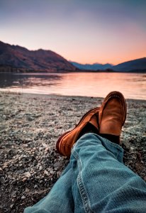 Person Wearing Blue Jeans And Brown Leather Loafers Sitting Beside Gray Sand photo