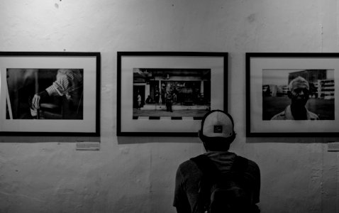 Grayscale Photo Of Man Wearing White Cap In Front Of Three Paintings photo