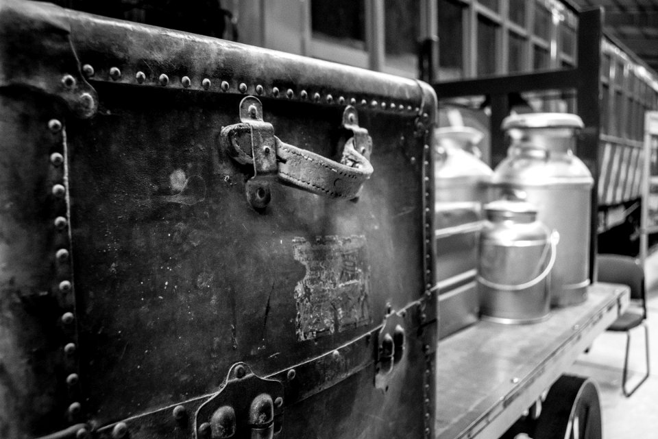 Grayscale Photography Of Travel Case With Milk Churns On Trailer