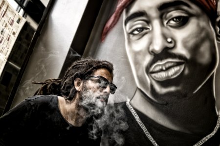 Man With Dreadlocks And Sunglasses Poses Near Tupac Shakur Portrait