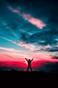 Silhouette Of Man Raising Hands Against A Red Sunset Light Under Green Clouds photo