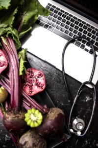 Macbook Pro With Stethoscope With Kiwi And Vegetables On Black Wooden Surface