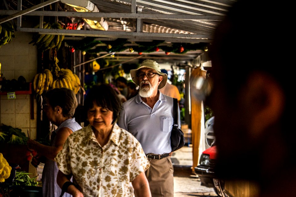 Man In Purple Polo Shirt And Brown Hat Behind Woman In Brown And White Floral Button-up T-shirt