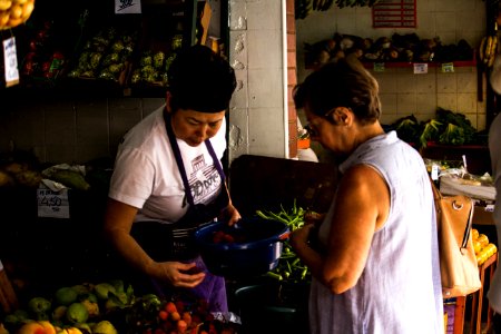 Photo Of Woman Holding Blue Bucket And Fruit Facing Woman Wearing Blue Sleeveless Shirt