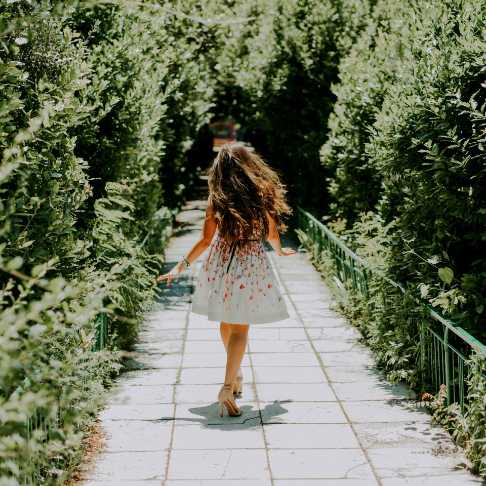 Photography Of Woman In White And Red Floral Midi Dress Walking On Pathway
