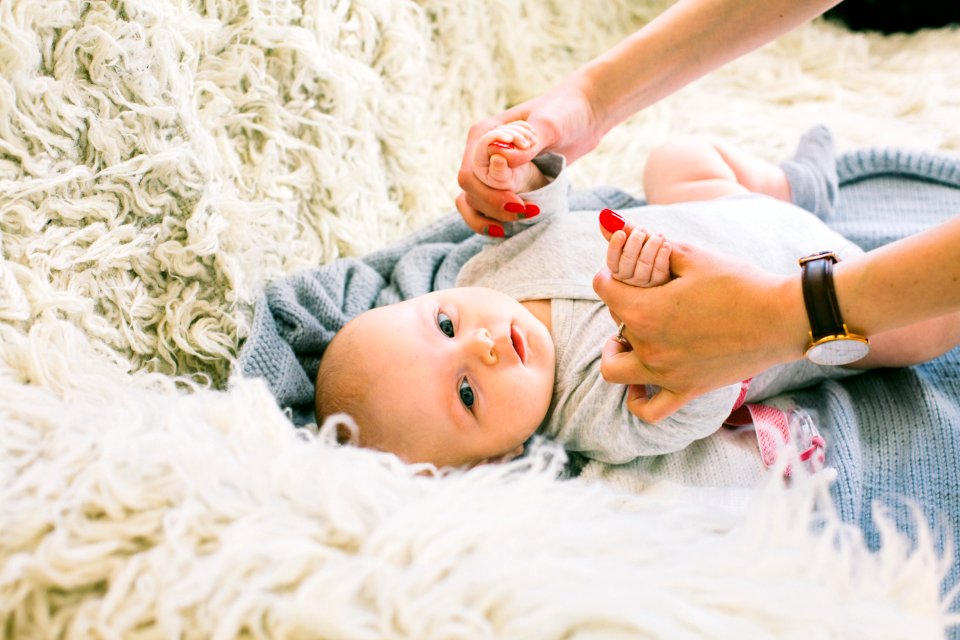 Baby In Gray Long-sleeved Onesie Lying On Beige Fur Textile