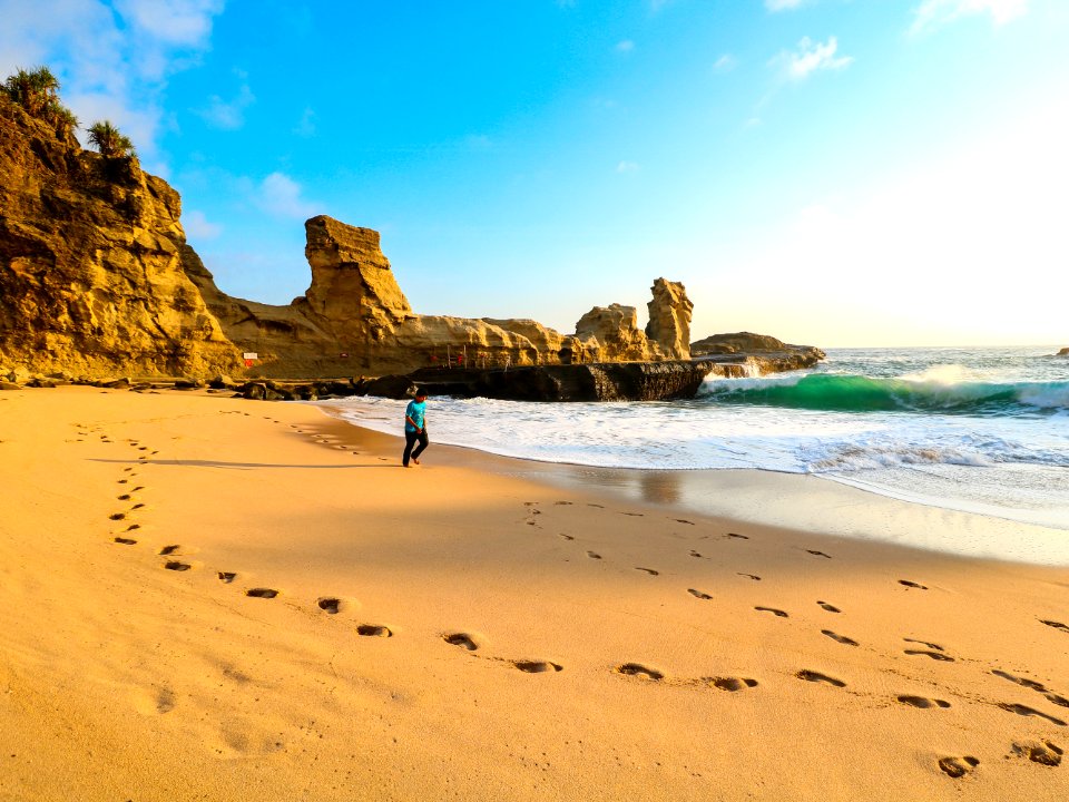 Person Walks On Brown Seashore Near Rock Formations
