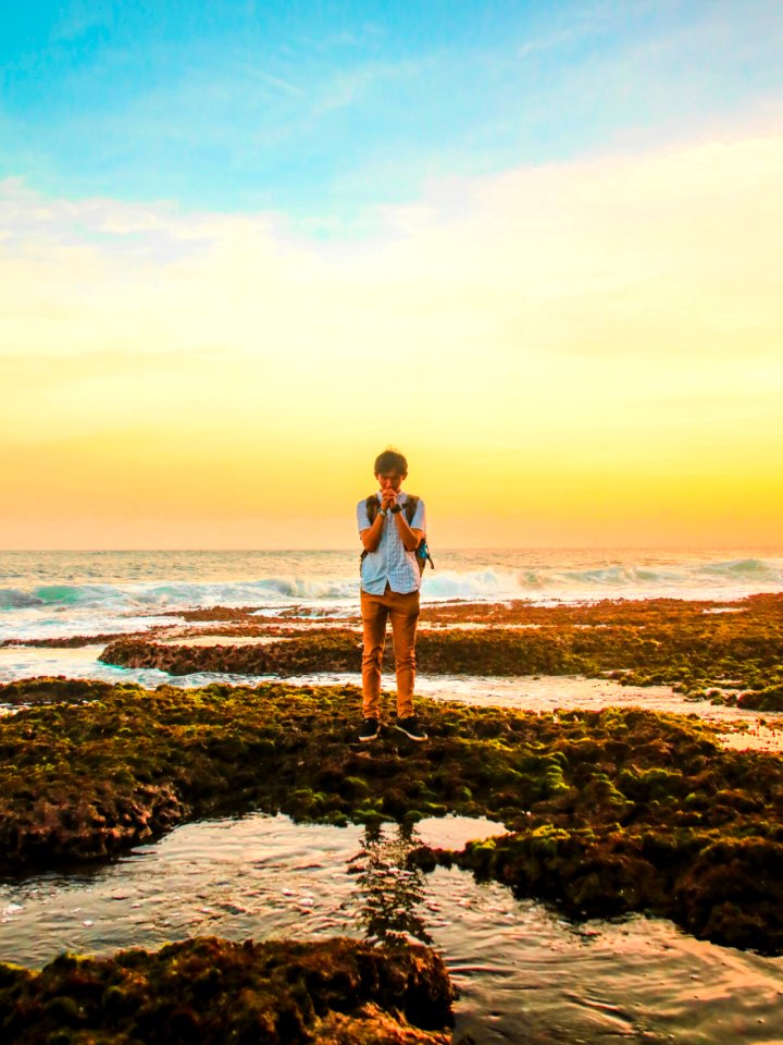 Man Standing On Rocks Near Beach During Golden Hour