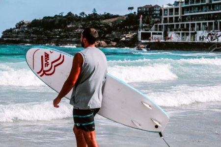 Man Walking Towards Body Of Water Holding A Surfboard photo