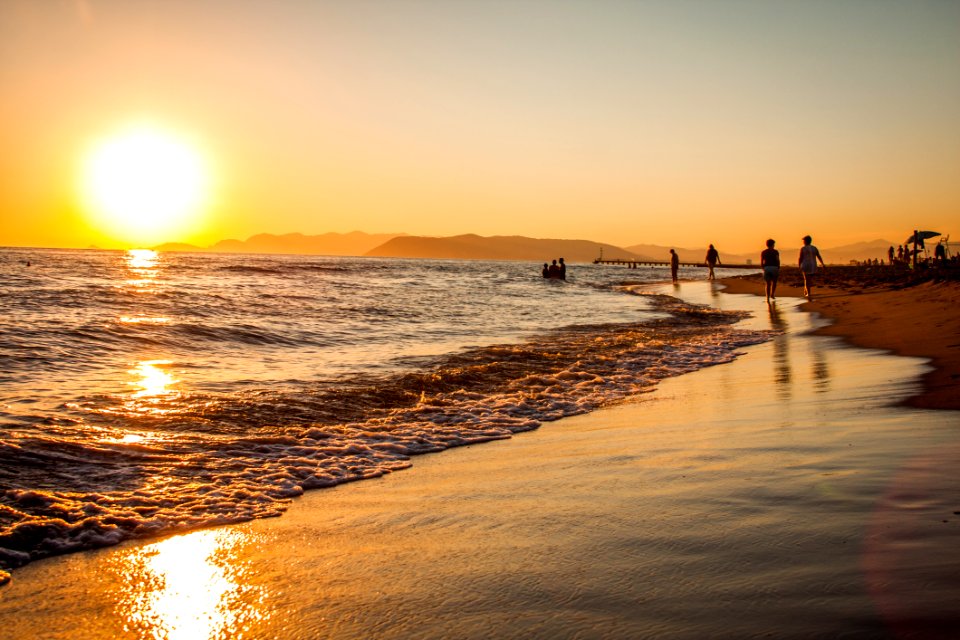 Group Of People Walking At The Shoreline During Golden Hour