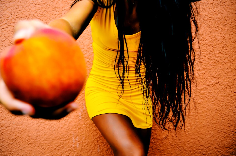 Woman Holding Round Fruit While Leaning On Orange Wall