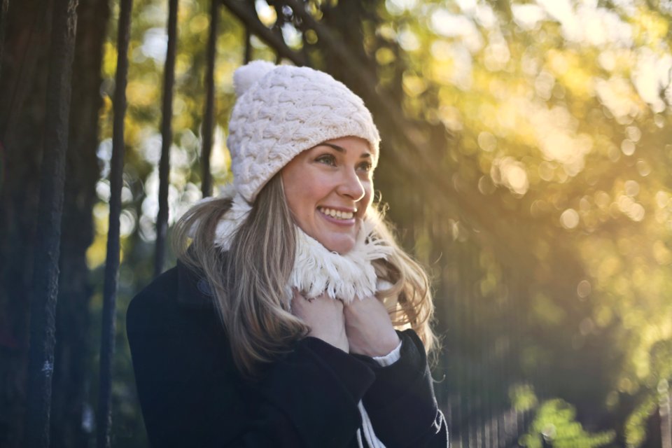 Photography Of Woman In Black Jacket And White Knit Cap Smiling Next To Black Metal Fence photo