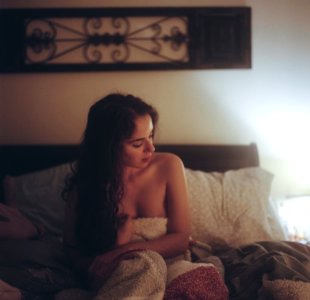 Topless Woman With White And Red Blanket On Bed With Pillows Under Brown Frame Inside White Painted Room photo