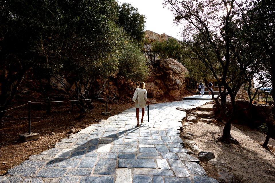 Woman Wearing White Top Holding Black Umbrella Walking On Cobblestone Pathway