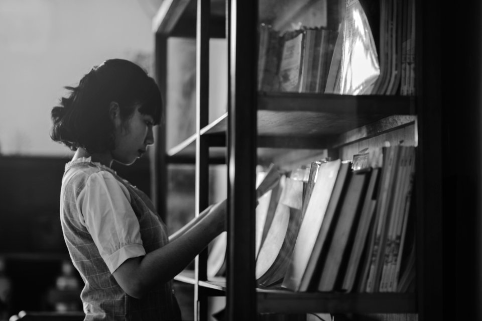 Grayscale Photo Of A Woman Holding A Book Inside The Library photo