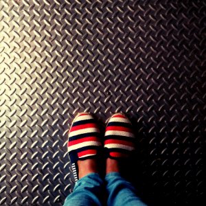 Person Wearing Red-and-multicolored Slip-on Shoes Standing On Gray Metallic Diamond Plate