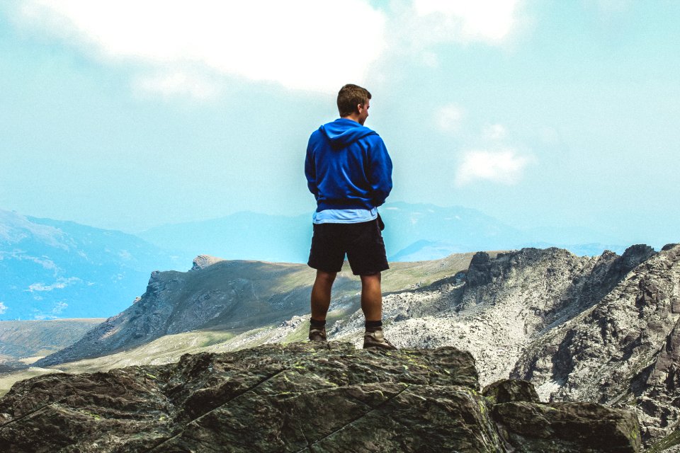 Man Wearing Blue Hoodie Standing On Top Of Mountain