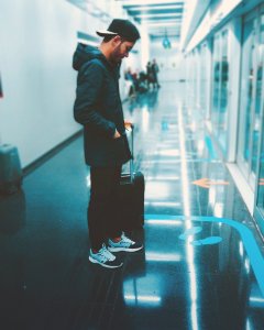 Man Stands Front Of Glass Panel While Holding Luggage photo