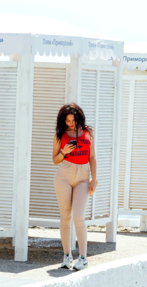 Woman In Red Tank Top And Gray High-waist Jeans Standing Near Wooden Cabinet