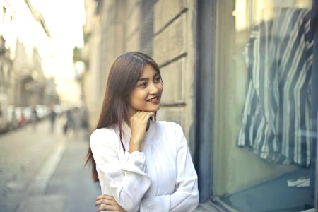 Focus Photo Of Woman In White Long-sleeved Dress Standing At The Front Of Gray Building