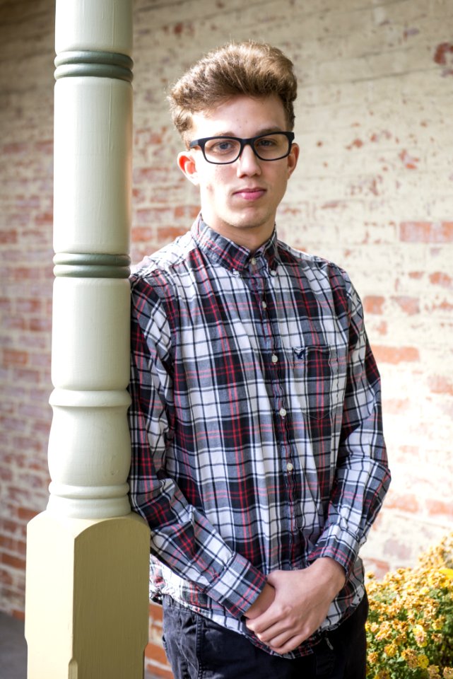 Man In Red Black And White Plaid-printed Dress Shirt Wearing Wayfarer Eyeglasses Leaning On White Wooden Post