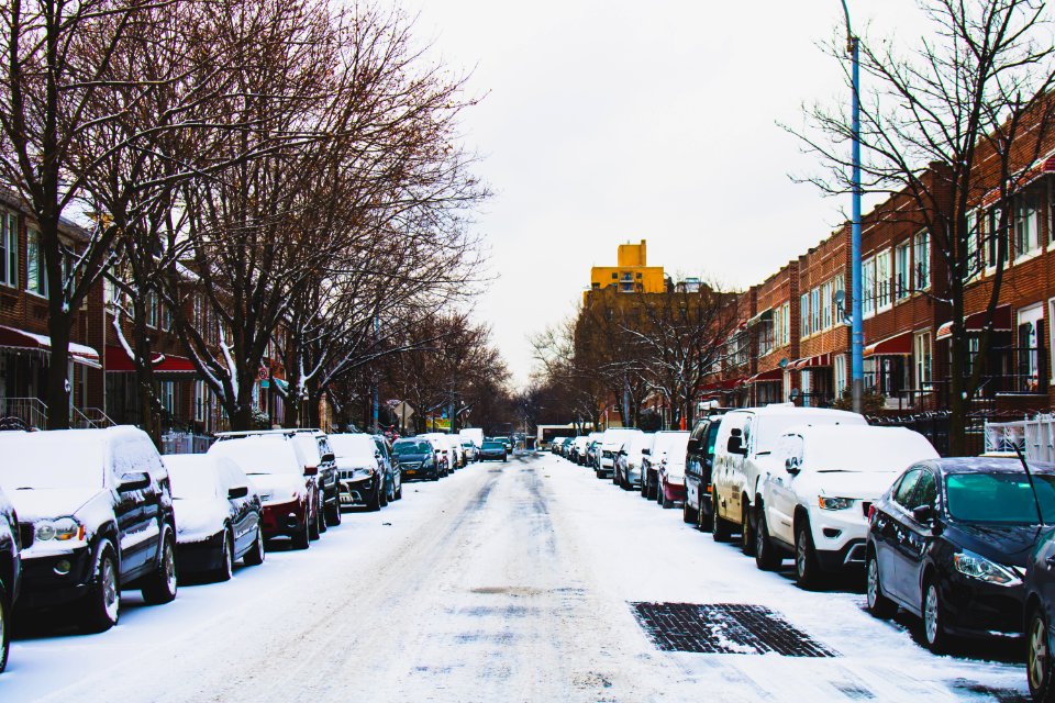 Snow Covered Road And Inline Parked Vehicles Between 2-storey Buildings Under White Sky