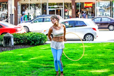 Woman In White Sleeveless Shirt And Blue Pants Holds Yellow Hula Hoop Stands On Green Grass