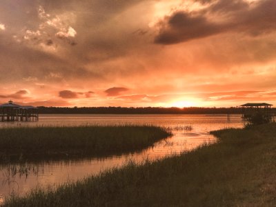 Grass Field Beside Body Of Water During Sunset