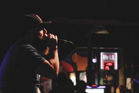 Man Wearing Grey Shirt And Black Cap Singing Using Corded Microphone photo