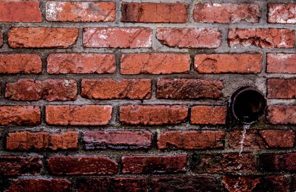 Round Brown Pipe Drainage With Liquid In Brown Bricked Concrete Wall