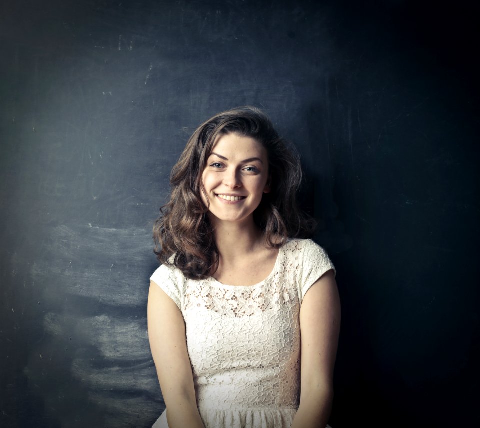 Brown Haired Girl In White Sleeveless Dress Standing Beside Black Painted Wall photo