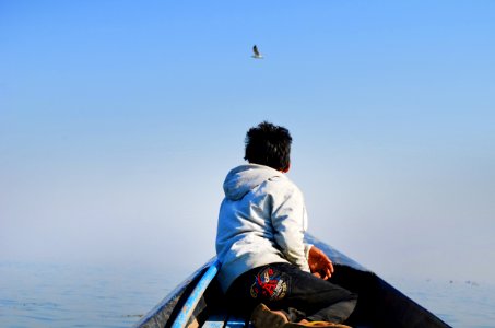 Man In Grey Hoodie And Black Pants Sitting In The Middle Of Boat Looking At Bird In The Sky photo