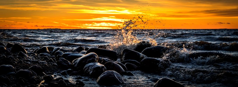 Waves Splashing At Stones On Beach During Sunset photo