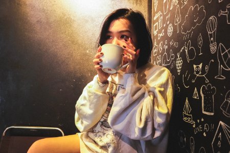 Woman Wearing White Over Shirt Holding White Ceramic Mug Beside Black Printed Wall