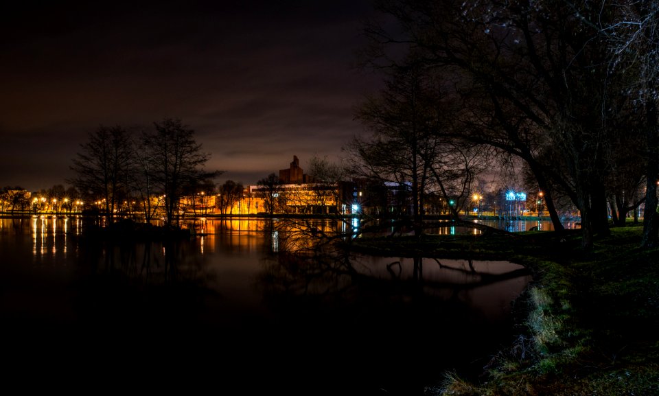 Still Body Of Water Next To Lighted Beige Buildings During Nighttime