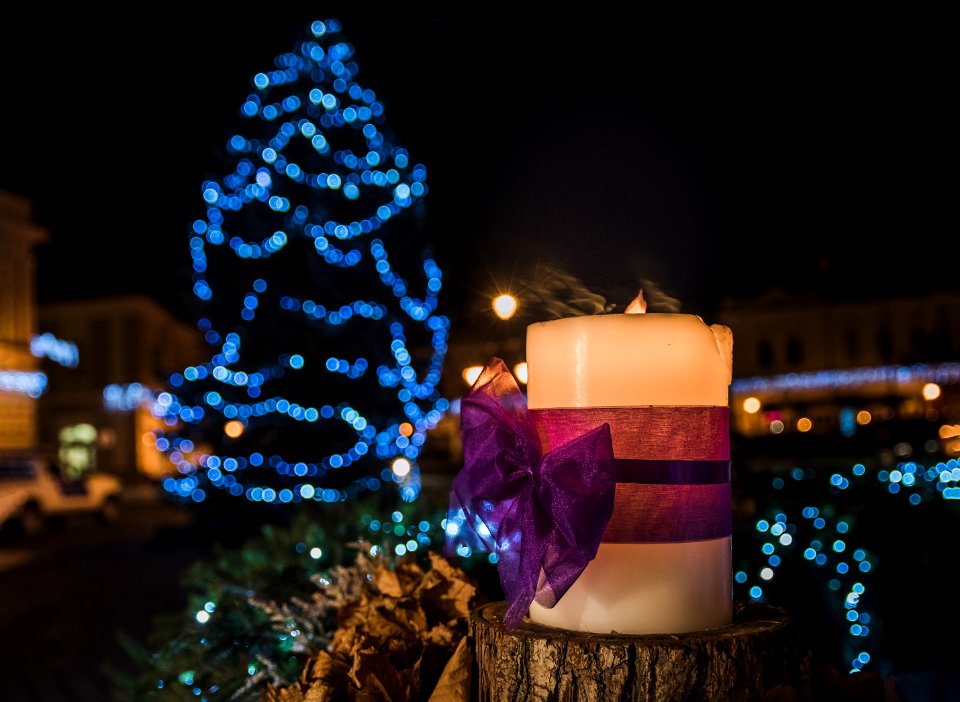 White Pillar Candle On The Log In A Distance Of Blue Led Light Christmas Tree