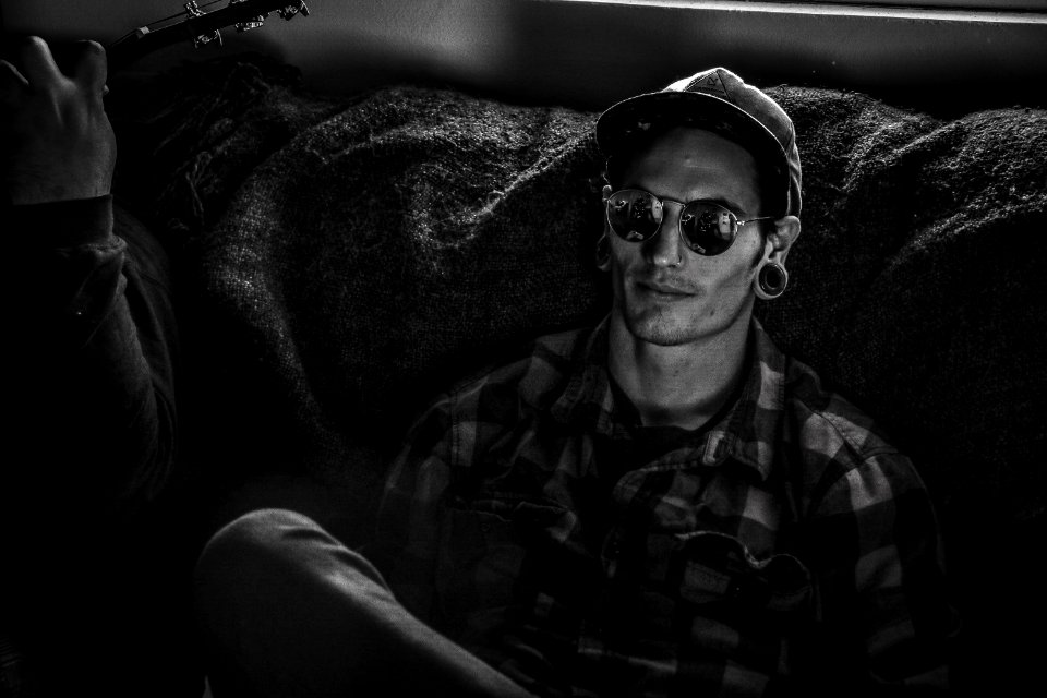 Grayscale Photo Of Man Wearing Snapback Cap And Plaid Dress Shirt Sitting On Couch photo